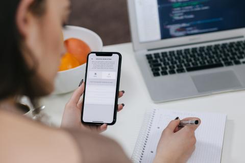 girl looking at cellphone and writing on notepad